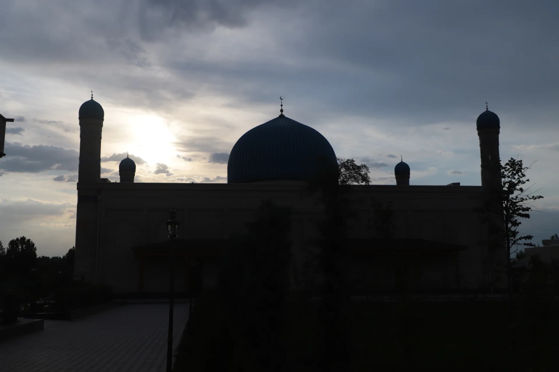 Silhouette of a large mosque with prominent domes and minarets against a cloudy sky
