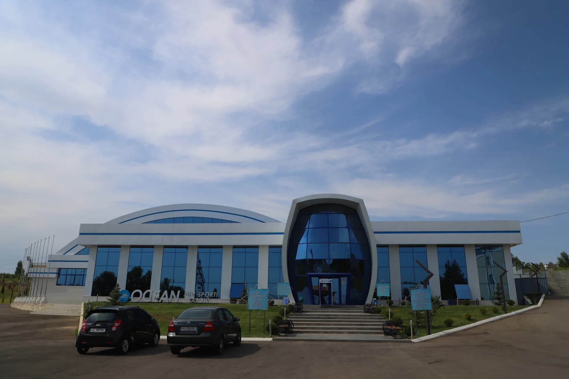 Modern sports building exterior with blue glass facade and parking area