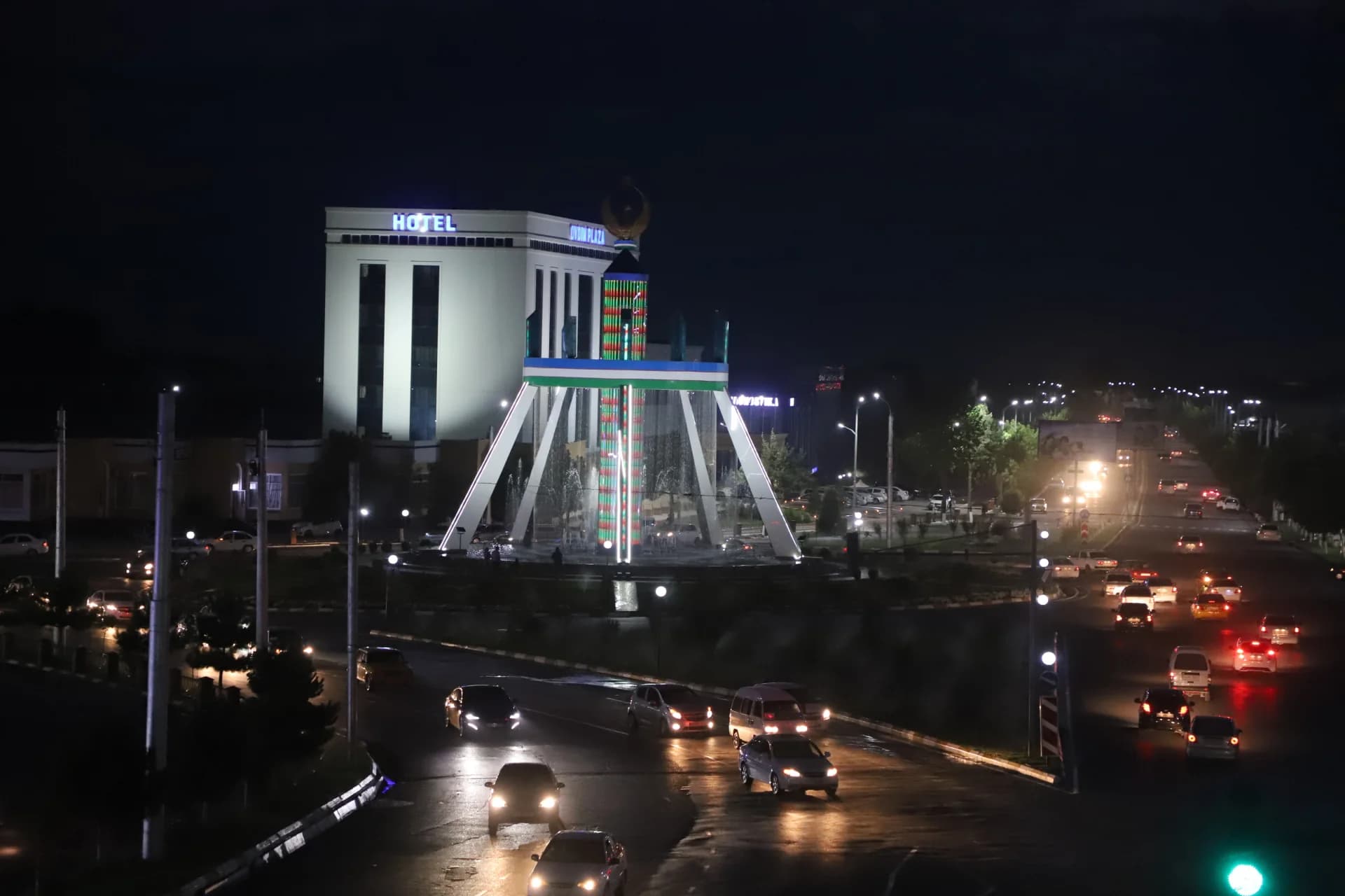 Night cityscape with illuminated fountain and vehicle traffic