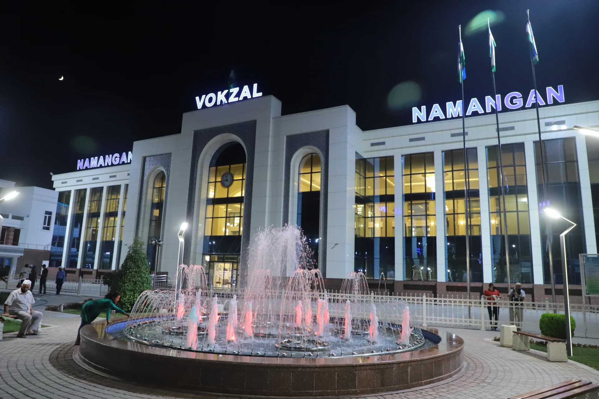 Illuminated railway station exterior at night with fountain