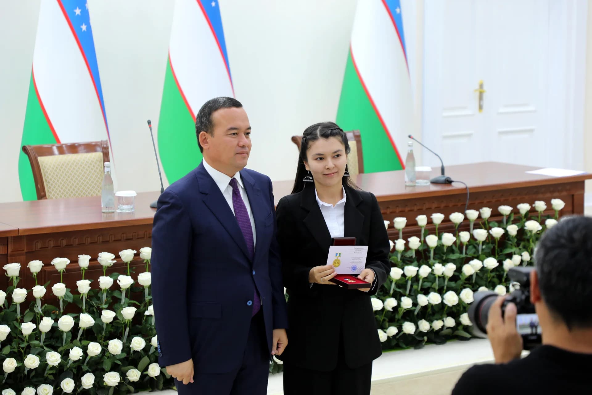 People posing for a photo near flags and white roses