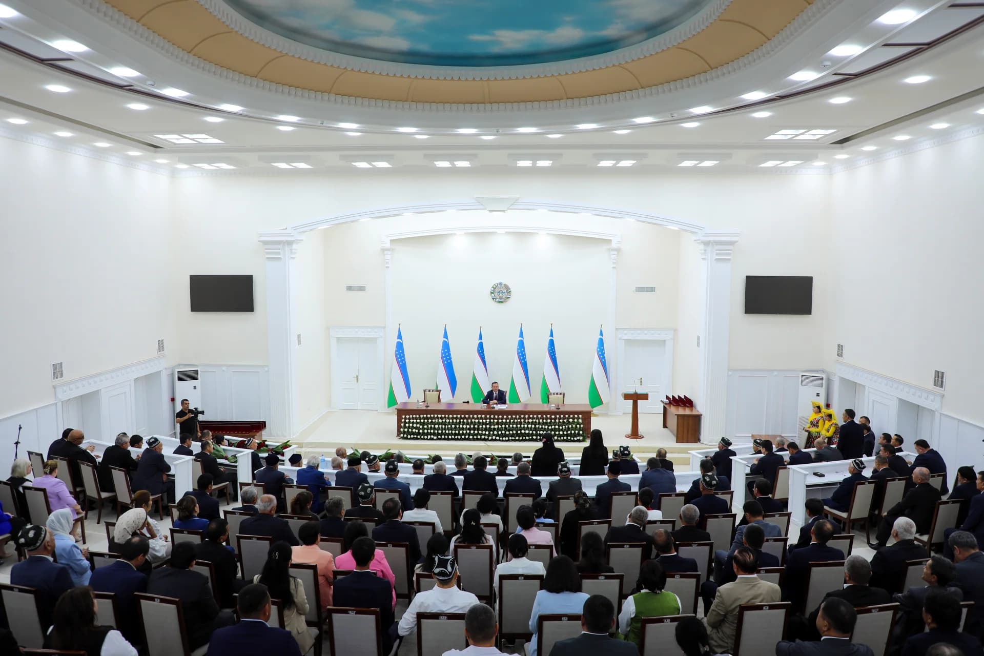 People gathered in a large meeting hall with national flags