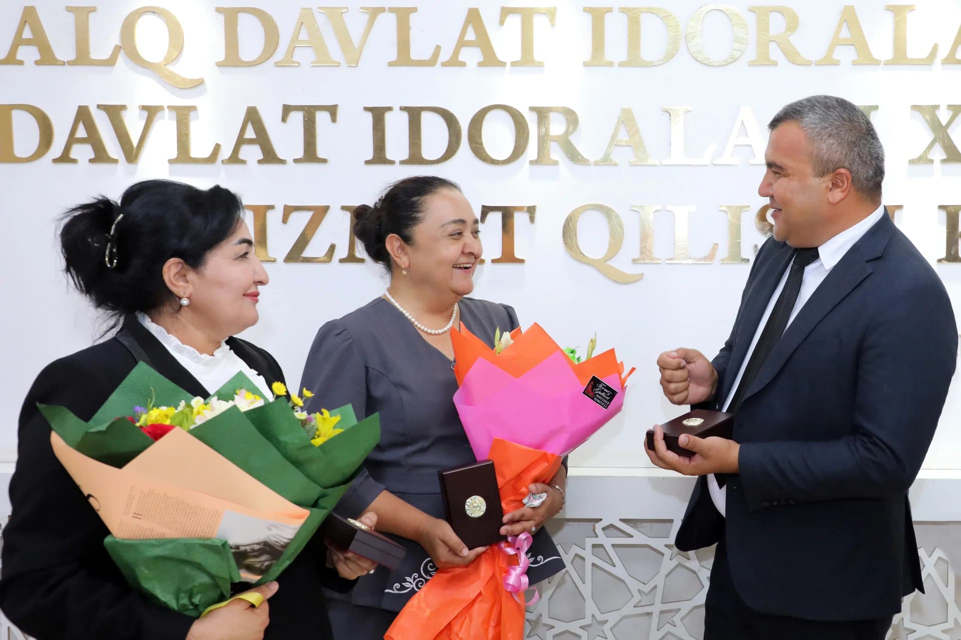 People holding flower bouquets and small gift boxes indoors