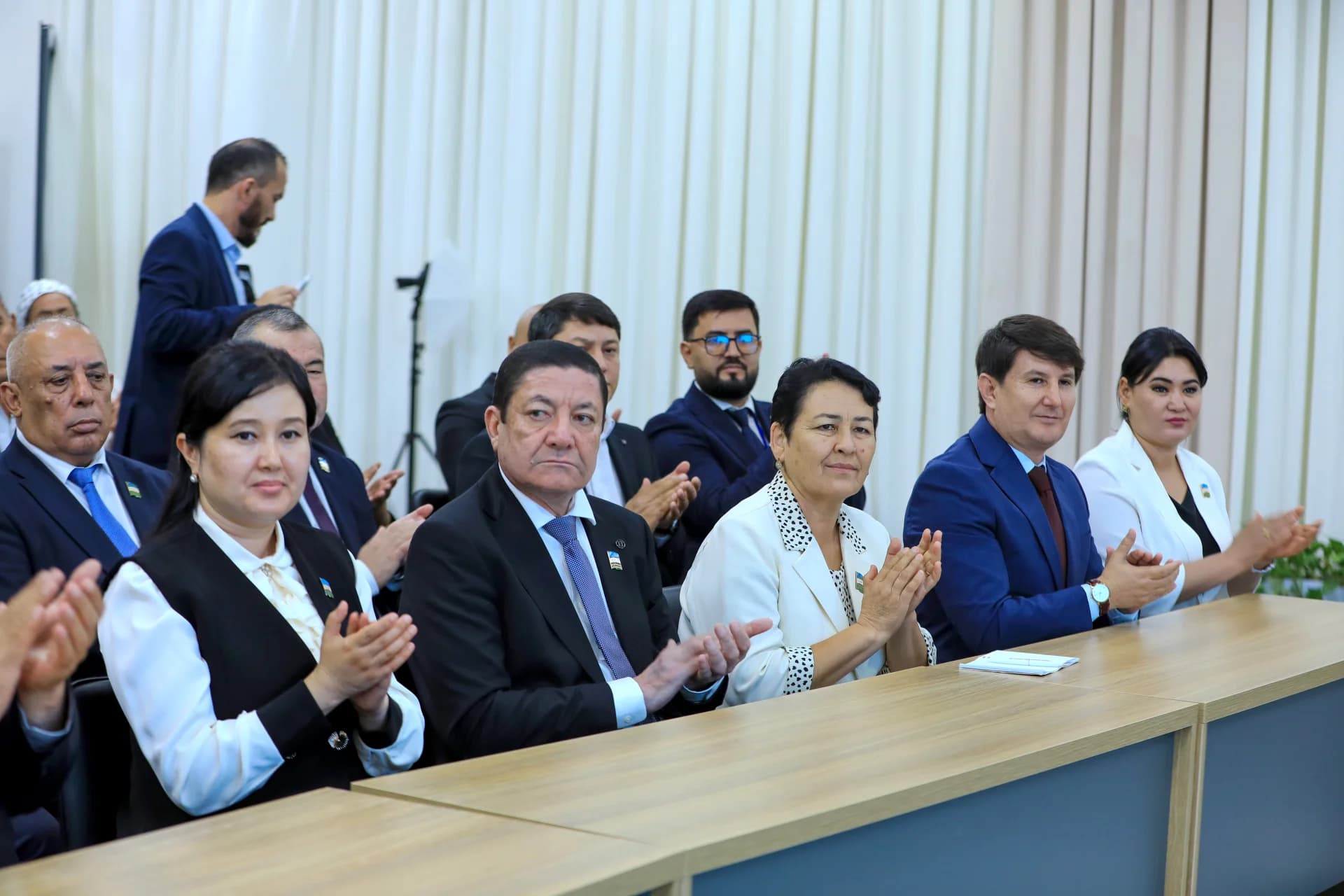 People seated at a table applauding in an indoor setting