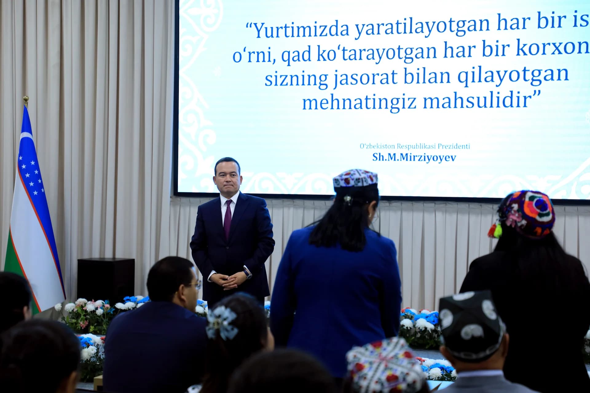 Man in suit addressing an audience in a hall