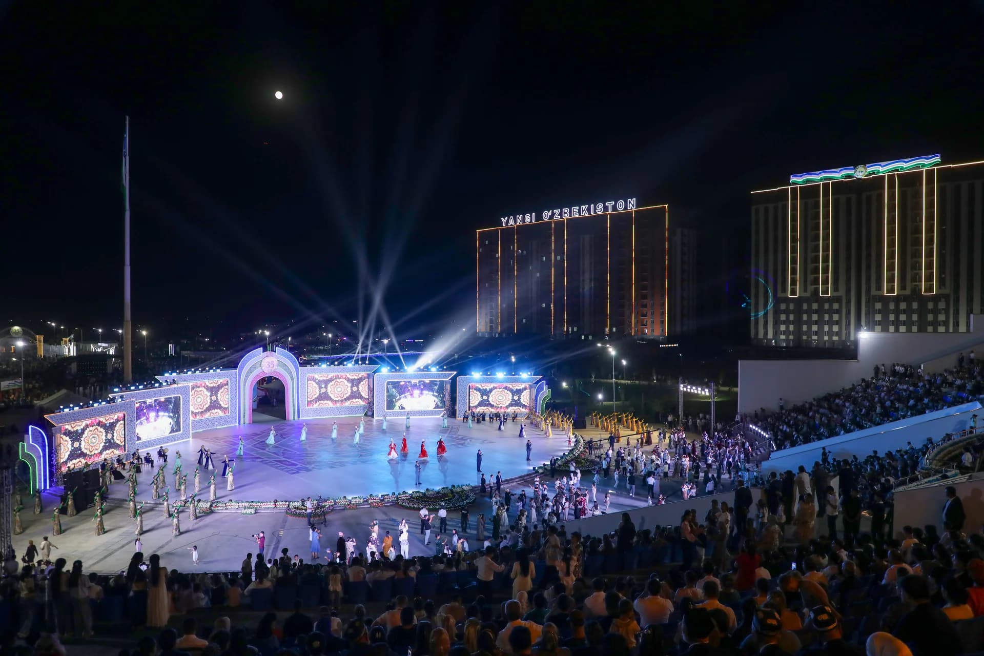 Performers on stage during an evening event with an illuminated building in the background