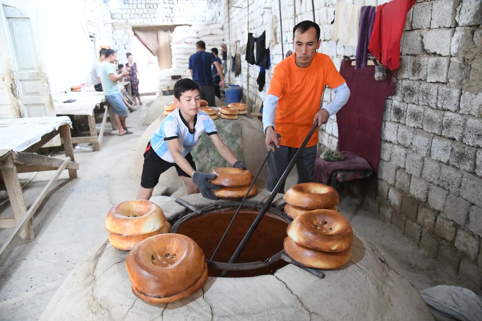 People baking flatbread in a traditional clay oven indoors