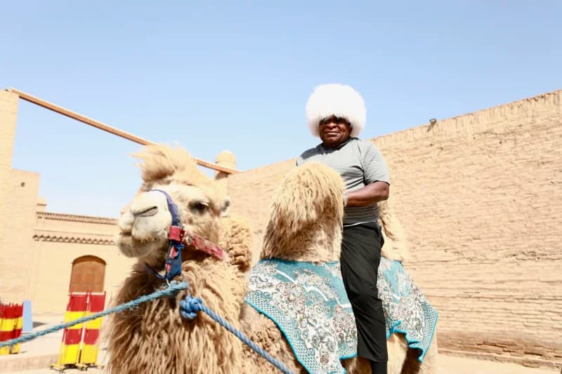 Man wearing white fur hat riding camel