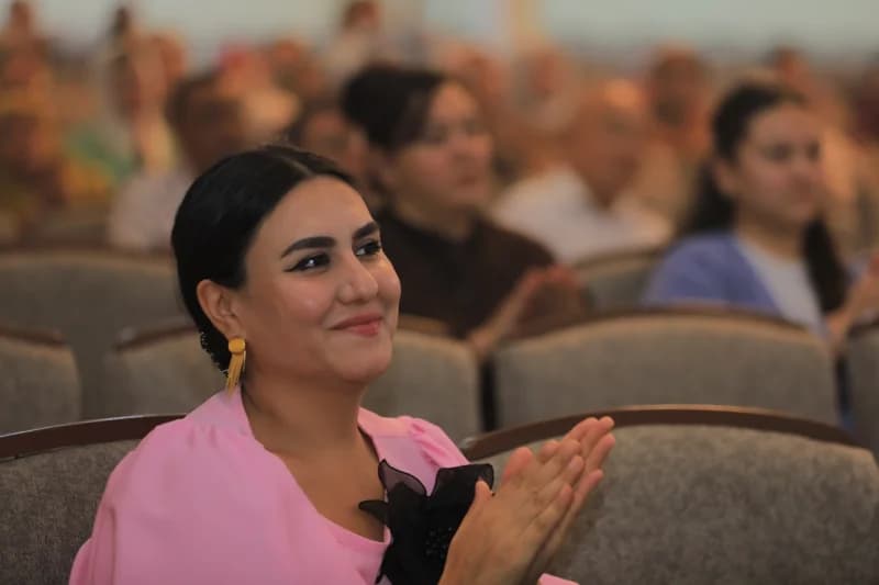 Auditoriyada tabassum qilayotgan va qarsak chalayotgan ayol