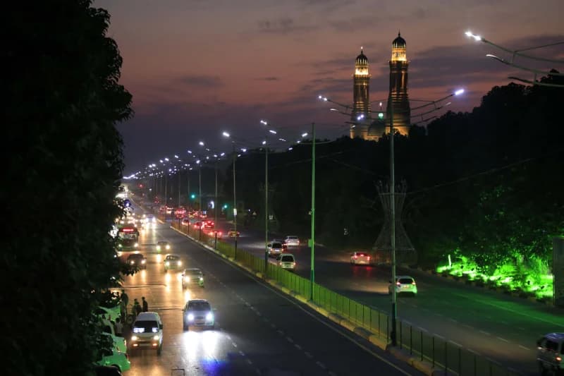 Urban traffic on a multi-lane road at dusk with illuminated minarets in the distance