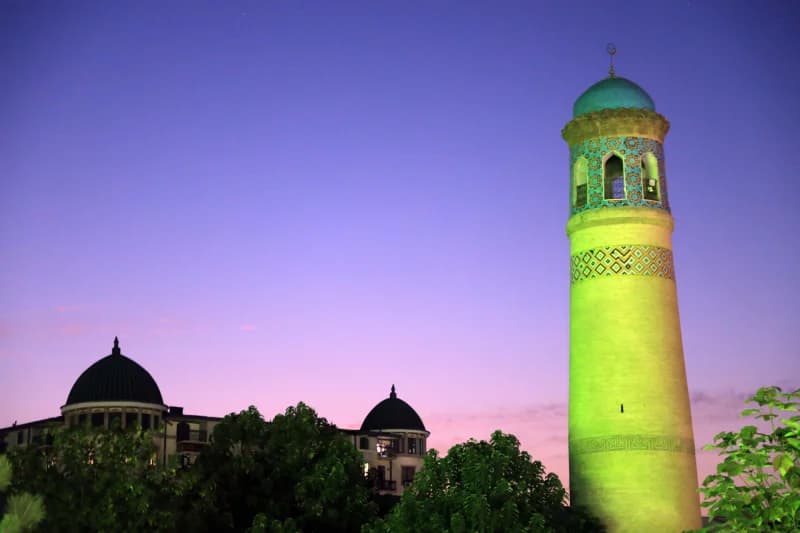 Illuminated minaret and building domes under a twilight sky