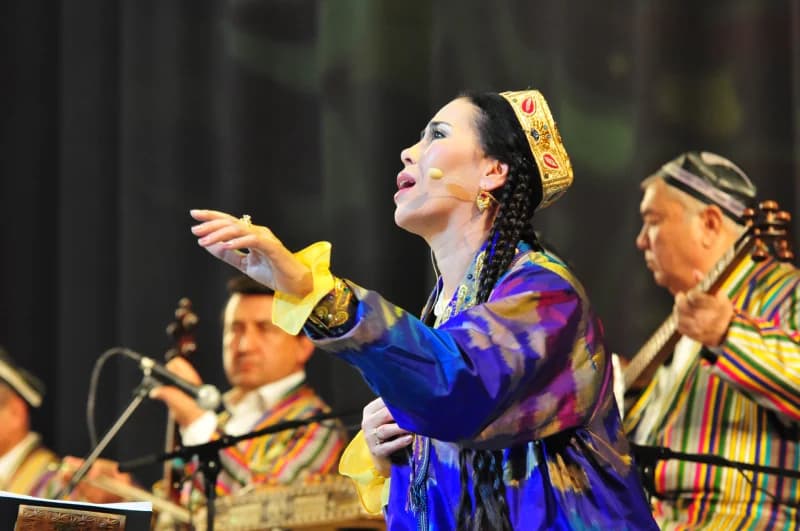 Anʼanaviy libosdagi ijrochi sahnada qoʻshiq kuylaydi