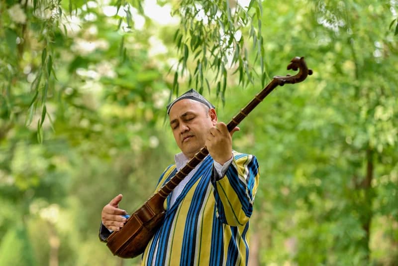 Ochiq havoda anʼanaviy torli cholgʻu chalayotgan odam