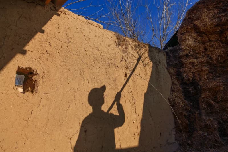 Shadow of a person holding a tool against a mud wall