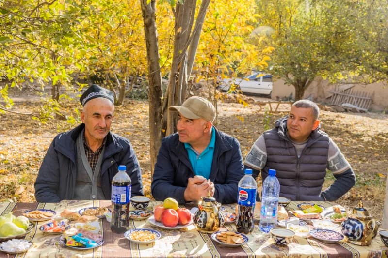 Three men sitting together outdoors at a table laden with food and drinks