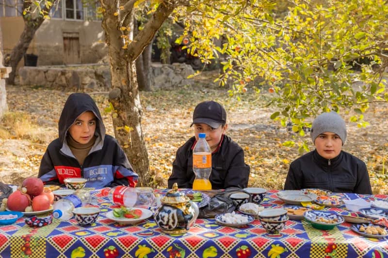 Three children sitting at an outdoor table with food