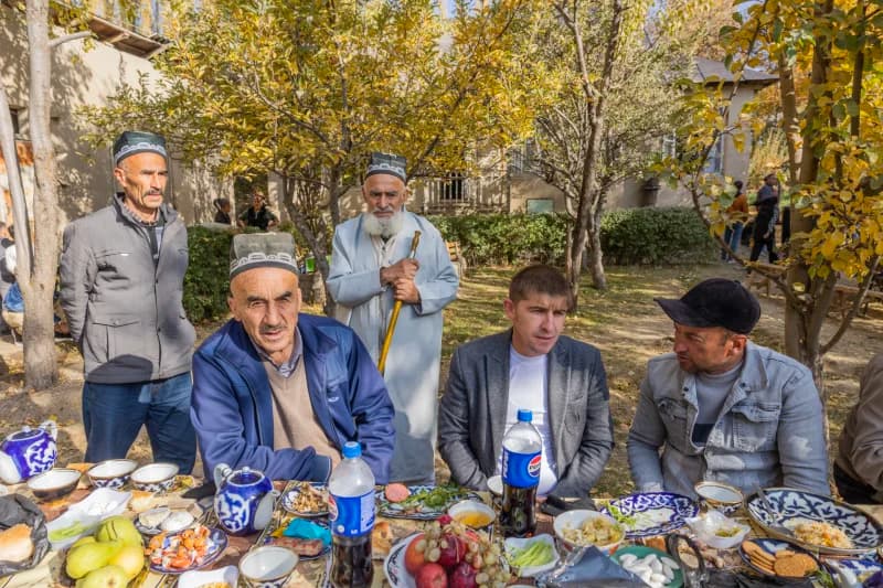Group of men gathered outdoors around a table laden with food and drinks