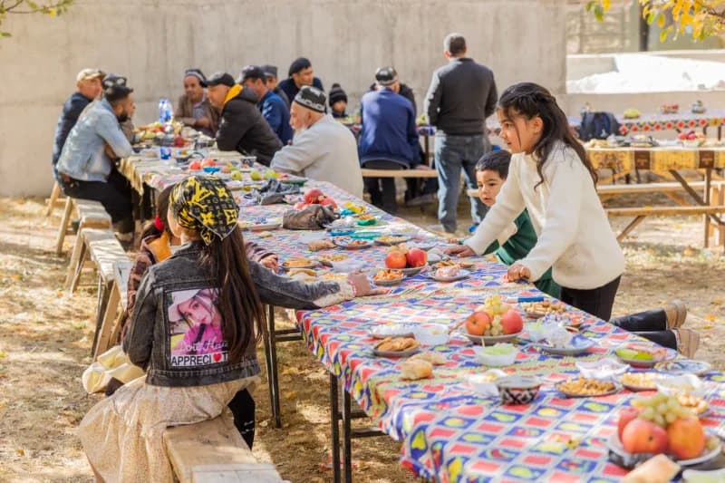 People gathered around long tables outdoors for a community meal