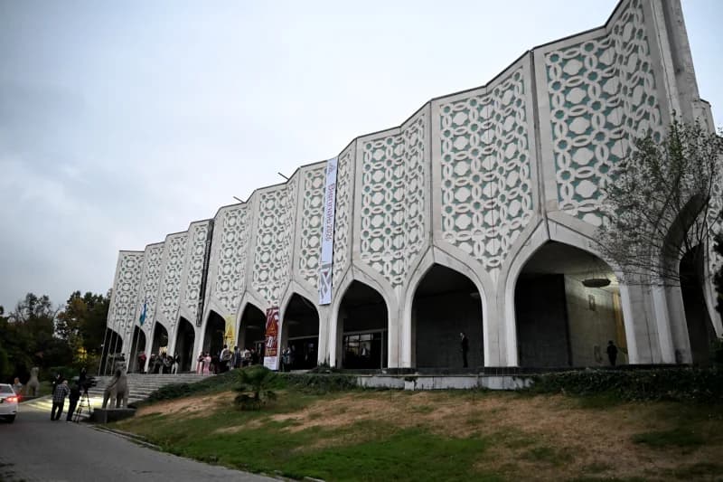 People stand outside a large building featuring patterned facade panels and arched entryways
